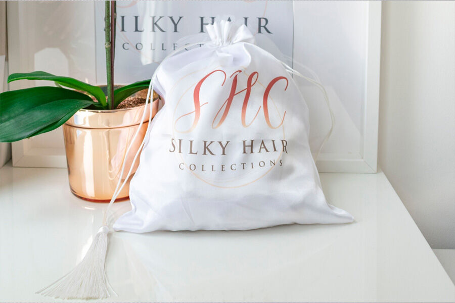 Белая атласная сумка на шнурке с фирменной символикой.