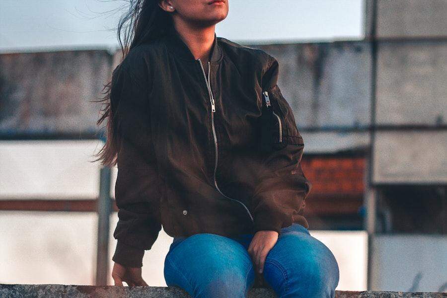 Женщина сидит на заборе в черной куртке бомбардировщика