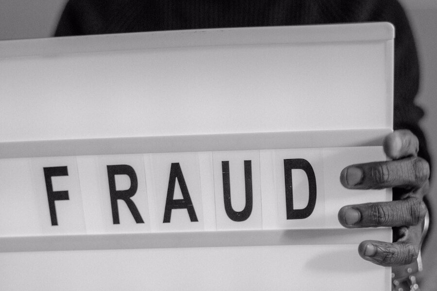 A man in handcuffs holds a sign that reads 'fraud‘