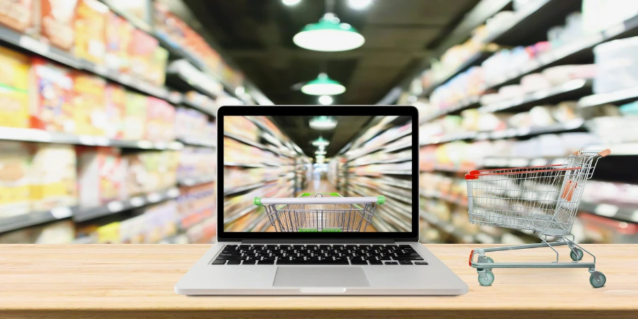 Supermarket aisle blurred background with laptops and shopping cart at wooden table for online shopping