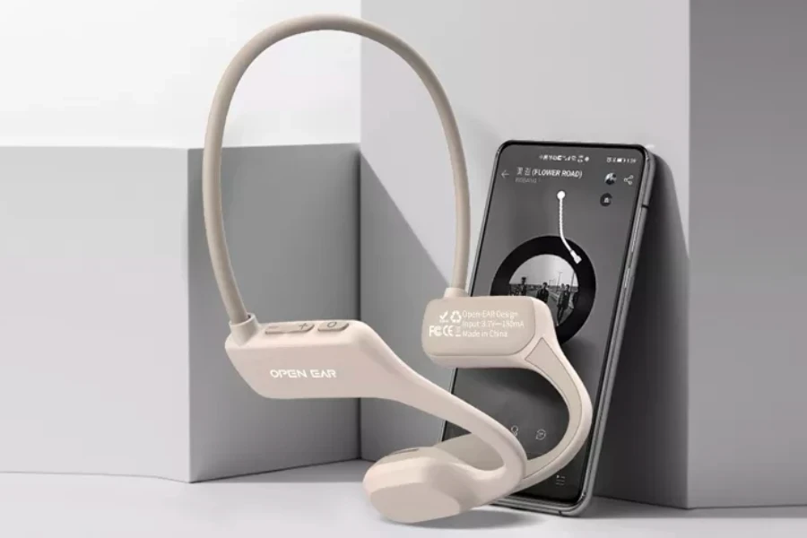 headphone konduksi tulang beige berdiri di depan smartphone