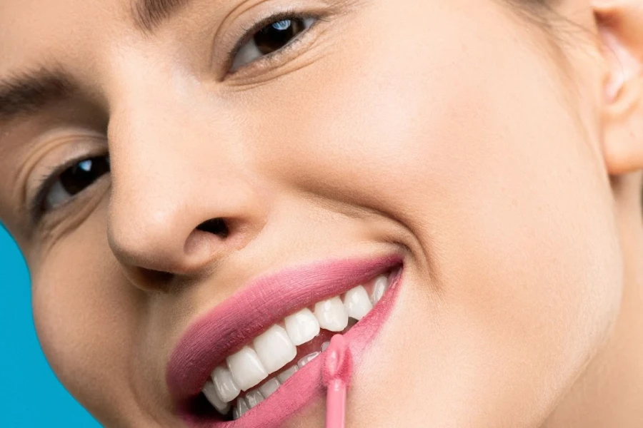 Девушка красит губы розовой помадой