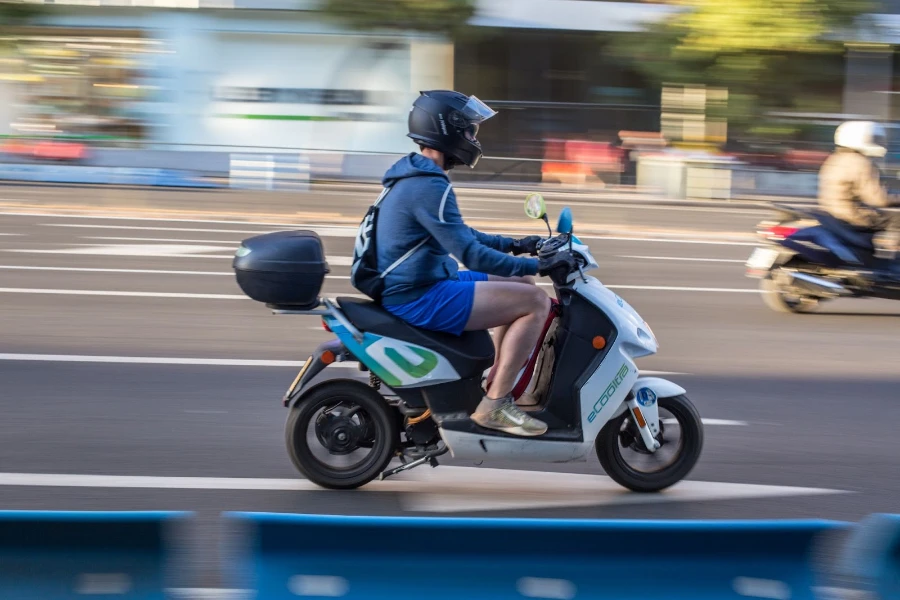 Yolda elektrikli motosiklet süren mavi ceketli adam
