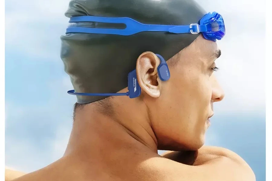 man wearing blue bone conduction headphones over a black swim cap and also wearing blue goggles
