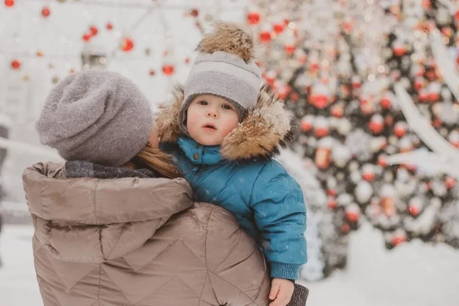 Mother carrying baby with gray pompom earflap winter hat