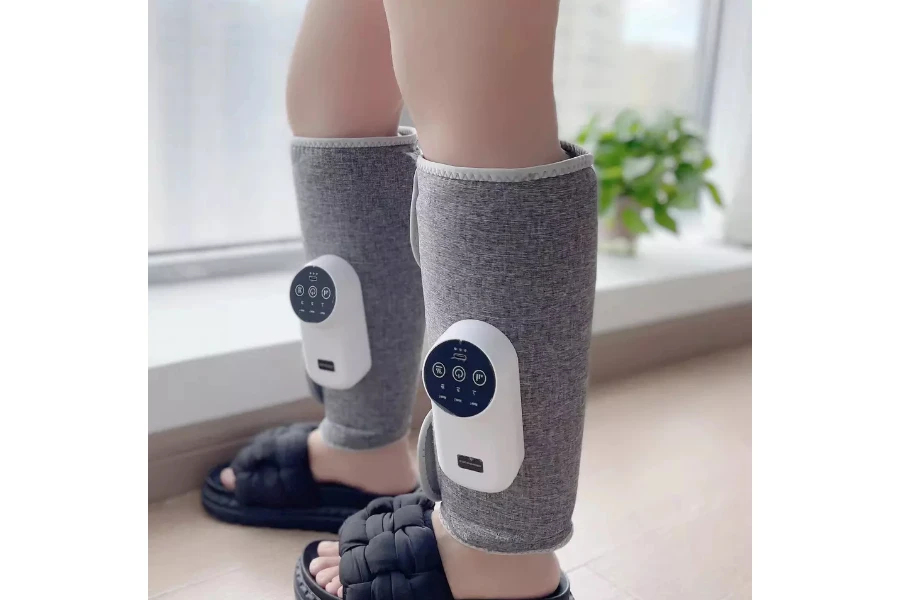 Her iki alt bacağına da elektrikli bacak masajı yapan kişi