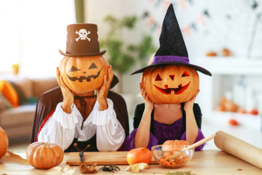two-people-holding-up-pumpkins-to-their-face-wearing-hats