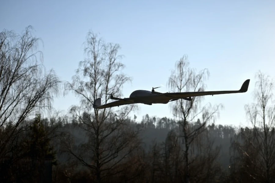 a fixed-wing drone flying in front of four birch trees