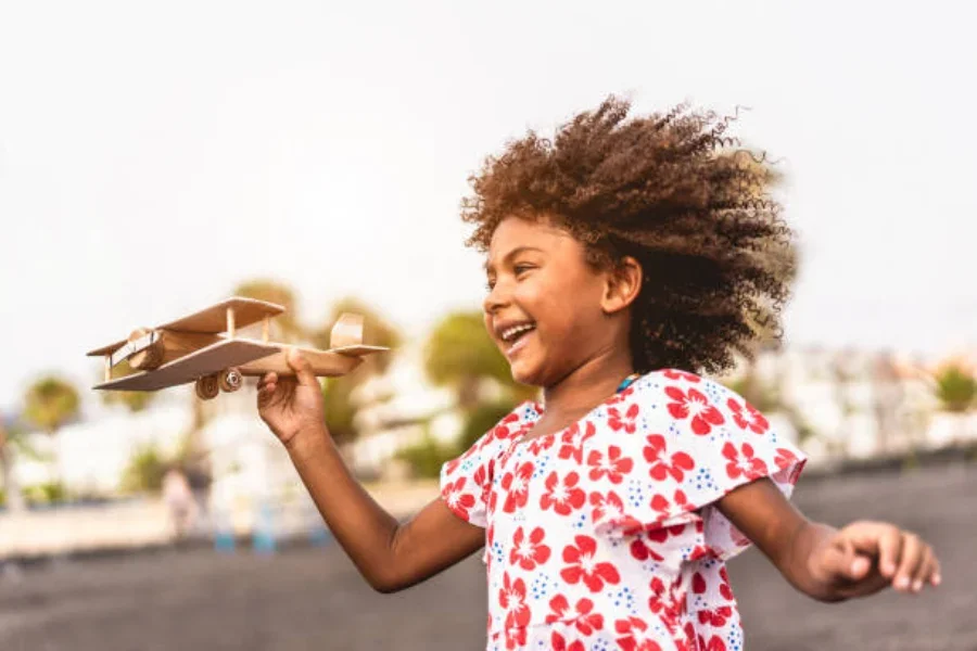 Little girl playing with a wooden toy airplane outside