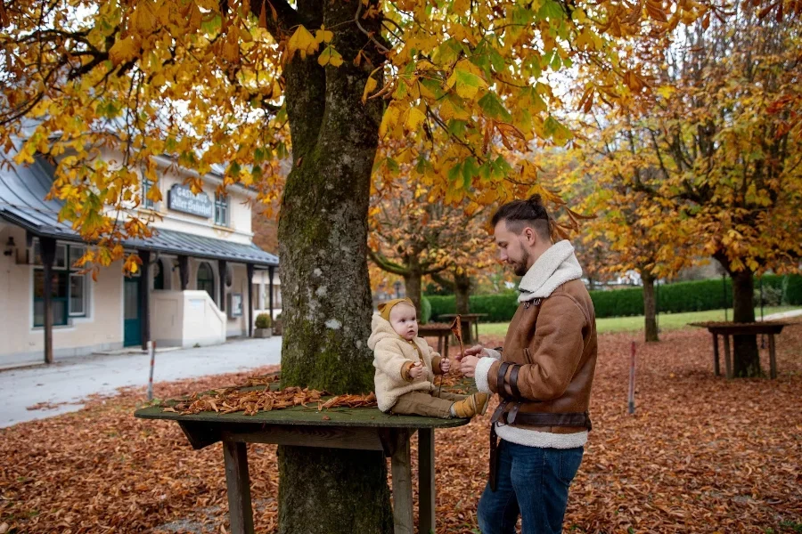Man in a wholegrain-colored coat playing with a baby