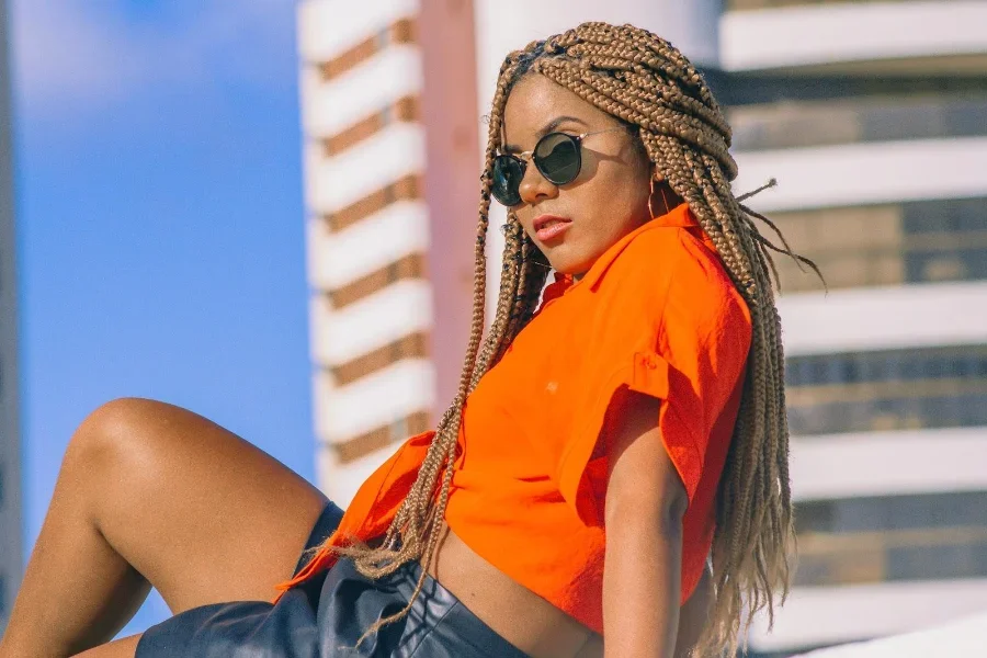 Wanita berkacamata hitam mengayunkan kemeja warna matahari terbenam yang berani