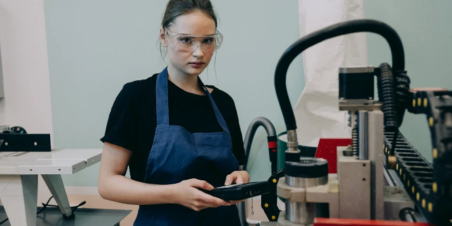 Young woman in safety glasses standing by a CNC machine