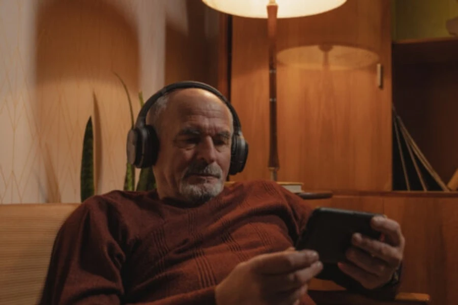 Pria tua dengan headphone memegang teleponnya