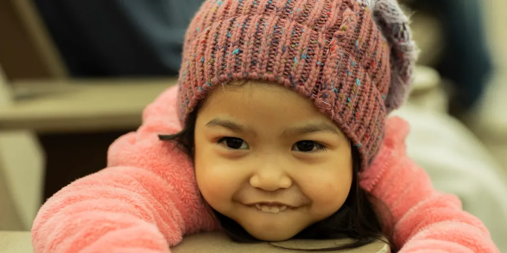 Girl smiling with a pink sweater and multi-colored beanie hat