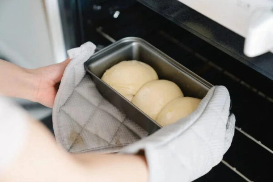 Person handling baked goods with oven mitts