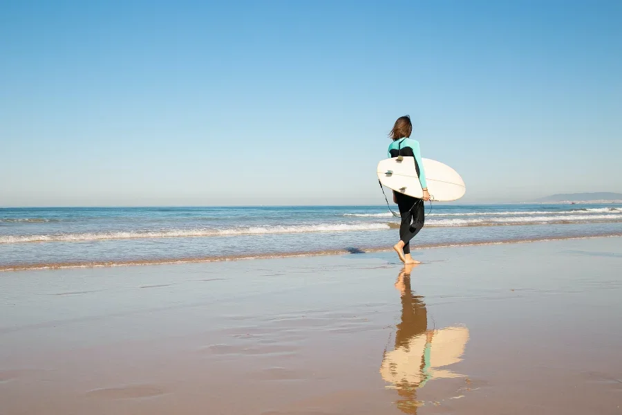 A woman in a buoyancy wetsuit carrying her surfboard
