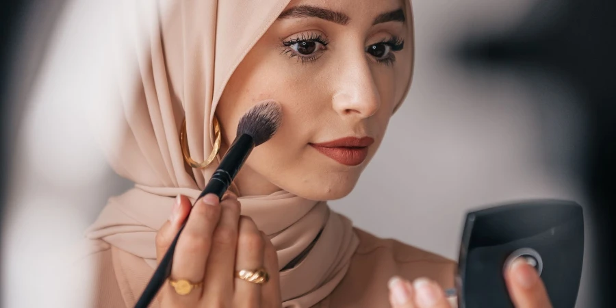 A woman wearing a hijab putting on blush