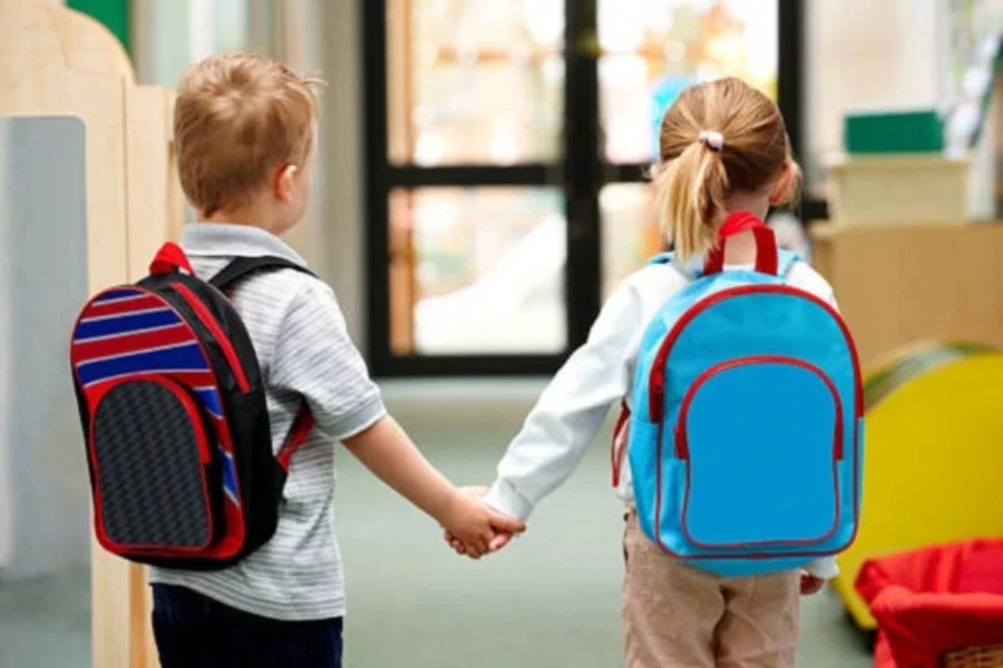 Niño y niña cogidos de la mano con mochilas impermeables en la escuela