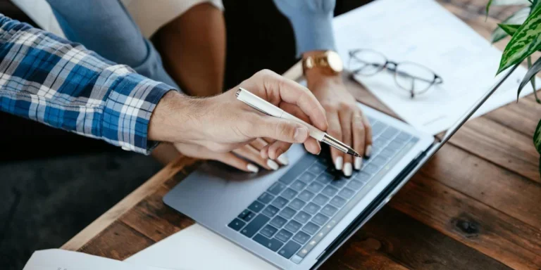Crop colleagues browsing laptop at table