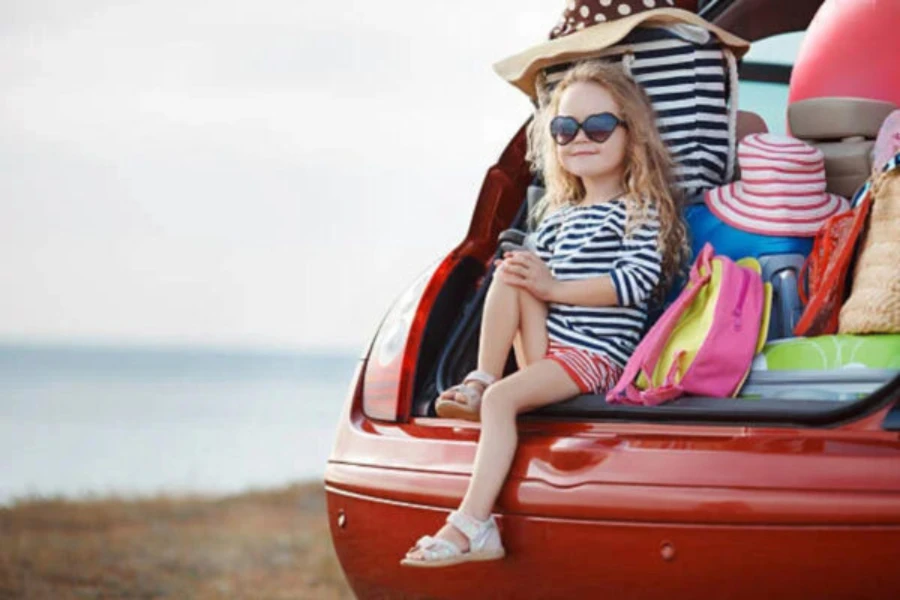 Mädchen sitzt im Kofferraum eines Autos mit Gepäck darin