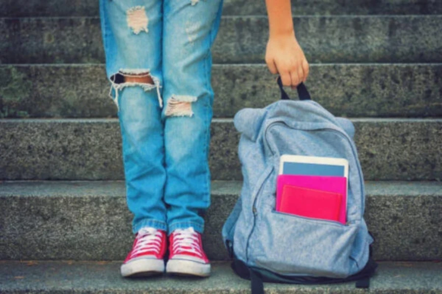 Chica de pie junto a una mochila azul con libros en el bolsillo