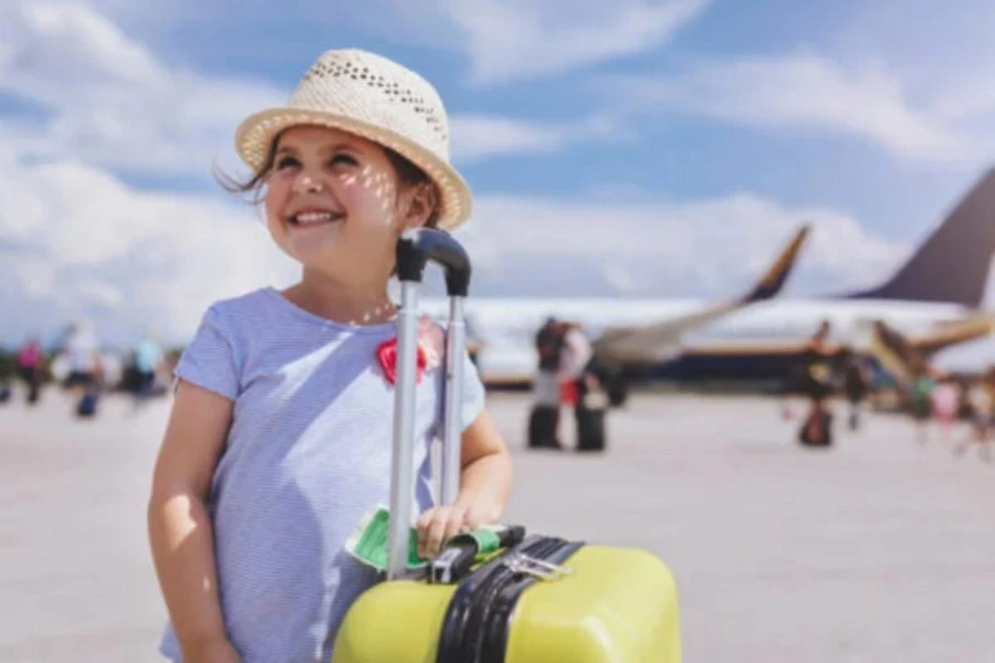 Girl wearing hat standing next to yellow suitcase on runway