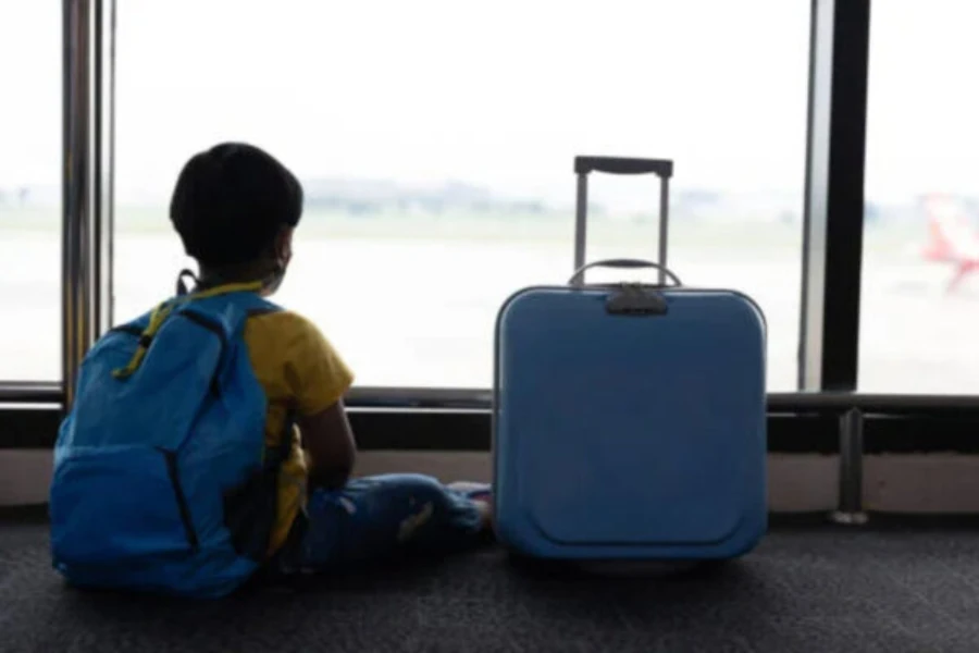 Kleiner Junge sitzt mit blauem Rucksack und Koffer auf dem Boden