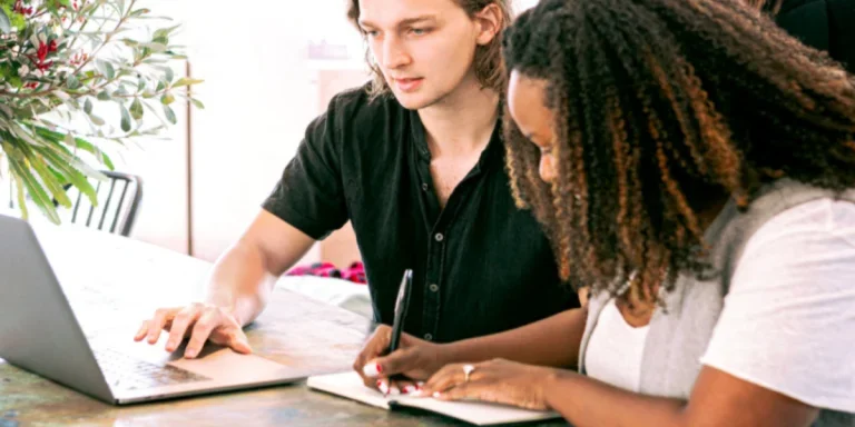 Man working on laptop while woman takes notes