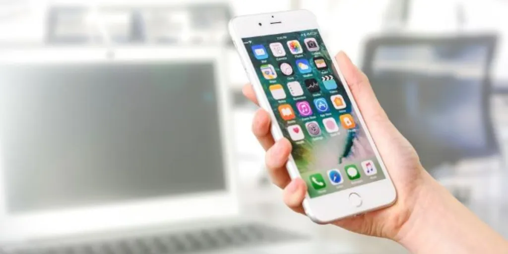 Jemand hält ein silbernes iPhone, auf dem einige Apps angezeigt werden