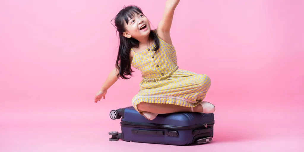 Young girl in a yellow dress sitting on blue suitcase