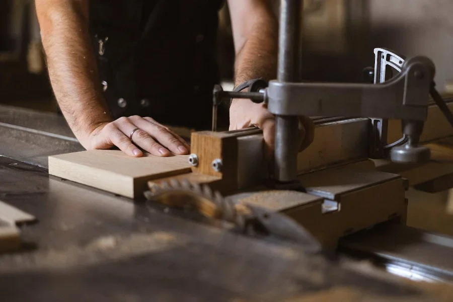 A man using an automated saw to cut a thick wooden lumber