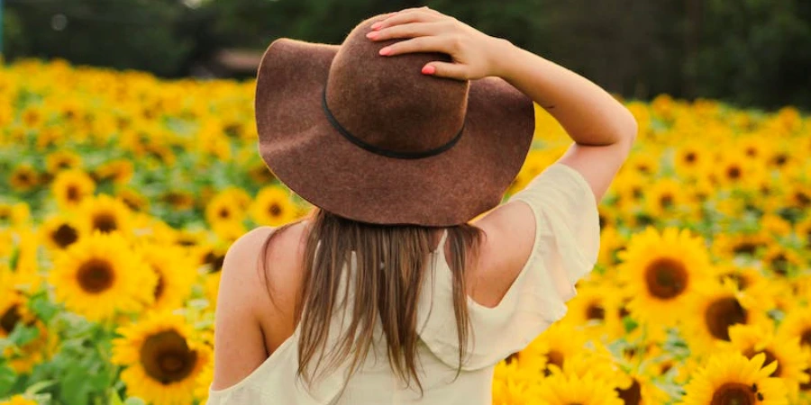 A woman standing in a field of sunflowers wearing a brow sun hat