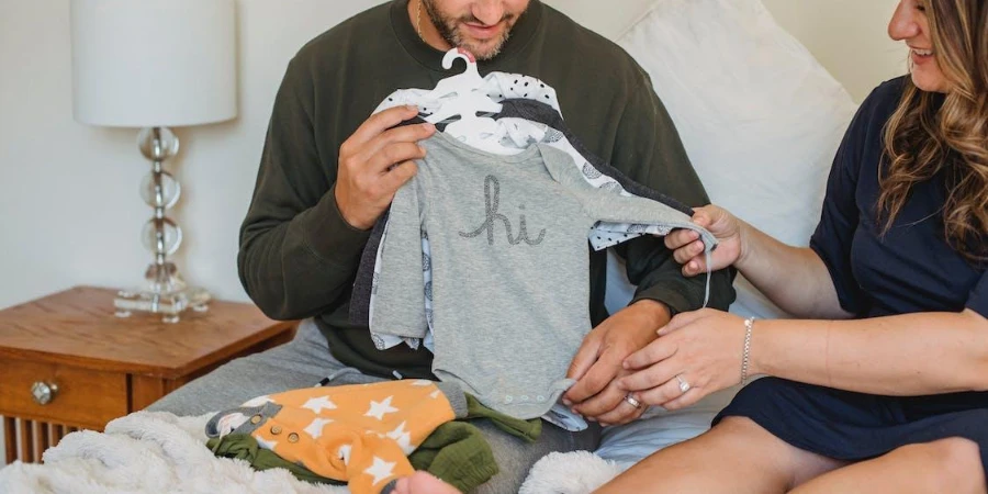 Two people holding some baby clothing sets