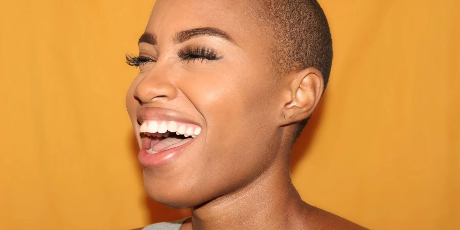 Woman with a shaved head and long eyelashes laughing