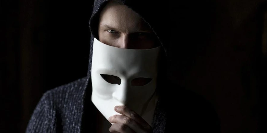 A man in black hoodie hiding behind a white mask