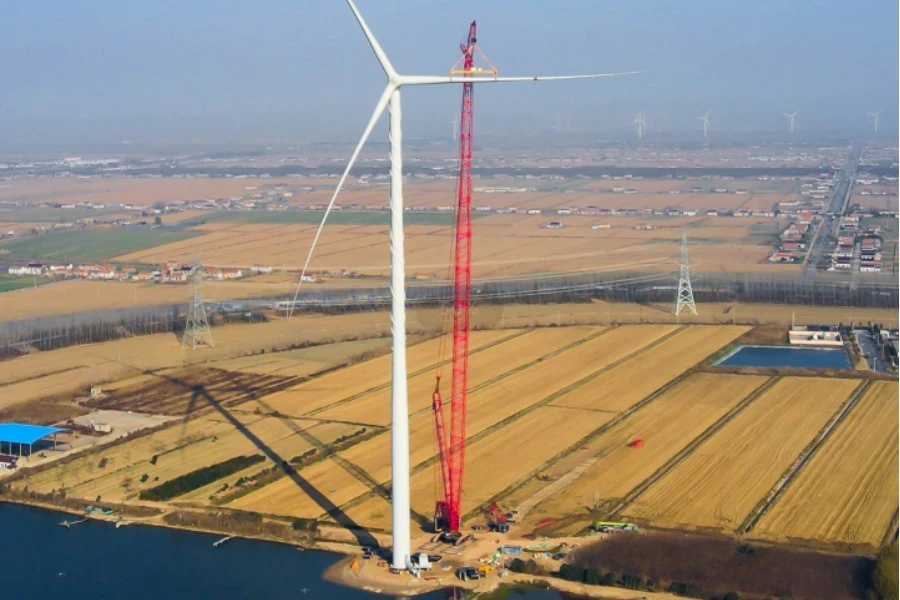 une grue sur chenilles soulevant une pale de ventilateur d'éolienne