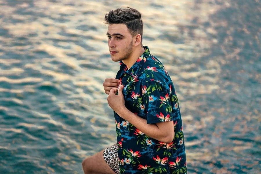 Um homem vestindo uma camisa floral sentado em uma praia