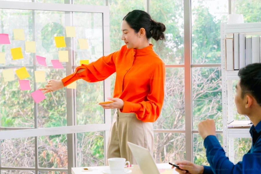 Lady sticking post-it notes to a window while her business partner looks on