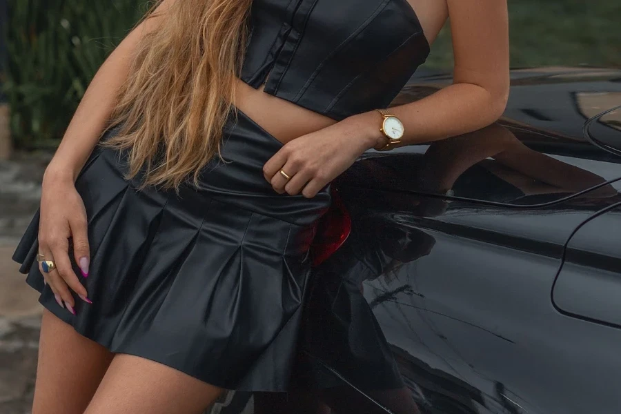 Lady wearing a pleated leather skirt resting on a car