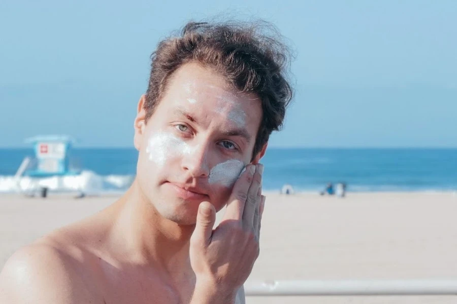 Mann trägt am Strand Sonnenschutzmittel auf sein Gesicht auf