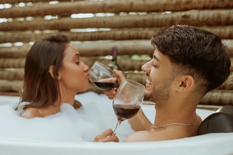 Мужчина принимает ванну и пьет вино со своим партнером