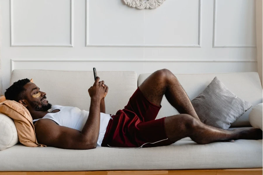 Man lying on the couch on his phone wearing under eye mask