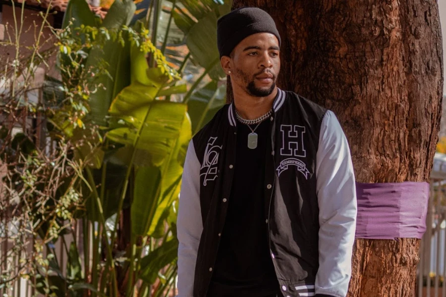 Man posing near a tree in a varsity jacket