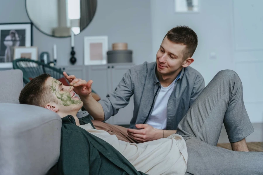 Mann setzt einem anderen Mann eine Gesichtsmaske auf