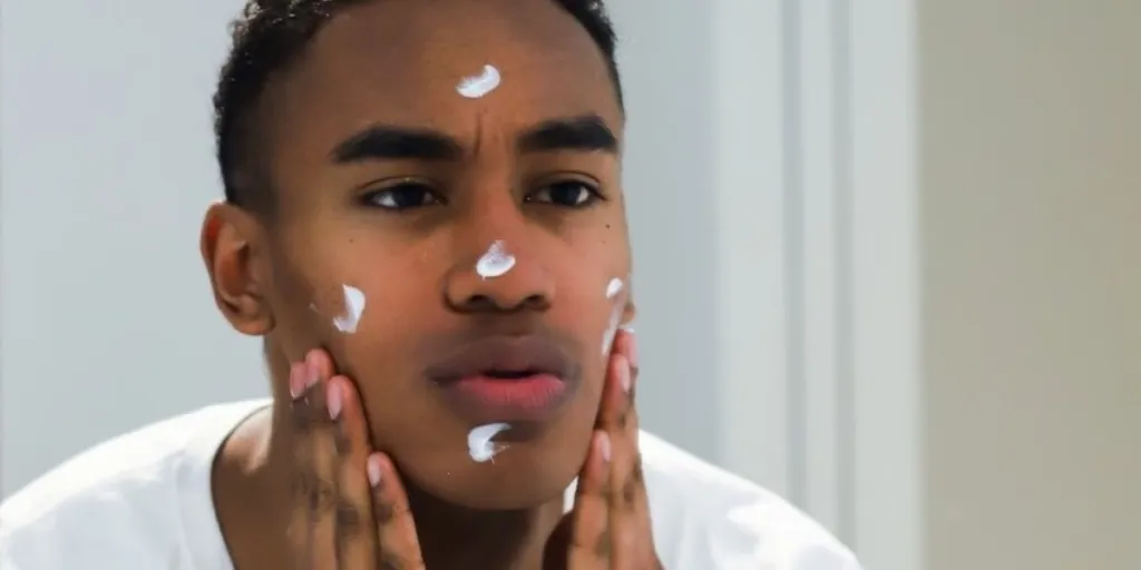 man putting moisturizer on his face in a mirror