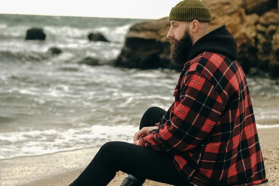 Mann sitzt am Strand und trägt ein rotes Flanellhemd