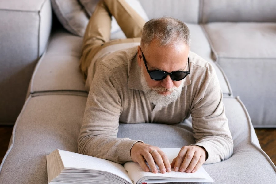 Older man laying on a couch reading a braille book