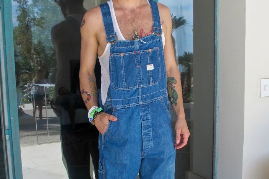 Tätowierter Mann, der Jeans-Mechaniker-Overalls rockt