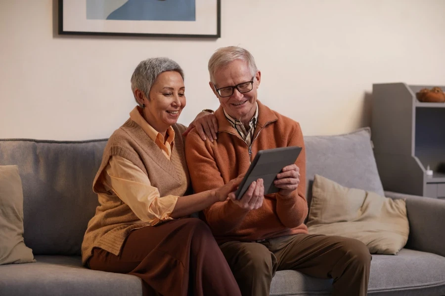 Dos personas mayores mirando y usando una tableta mientras están sentadas en el sofá