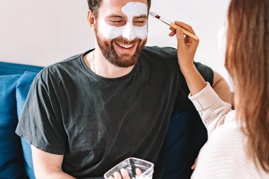 Frau trägt einem Mann eine Gesichtsmaske auf